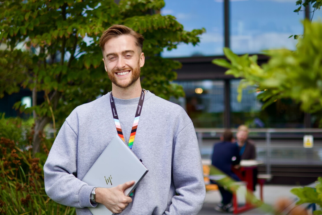 Smiling person holding HP laptop outdoors with rainbow lanyard
