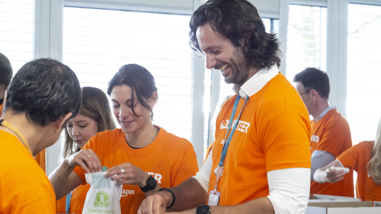Mehrere Amazon Mitarbeiter:innen in orangenen Volunteer T-Shirts beim Packen von Hygienesets für bedürftige Geflüchtete.