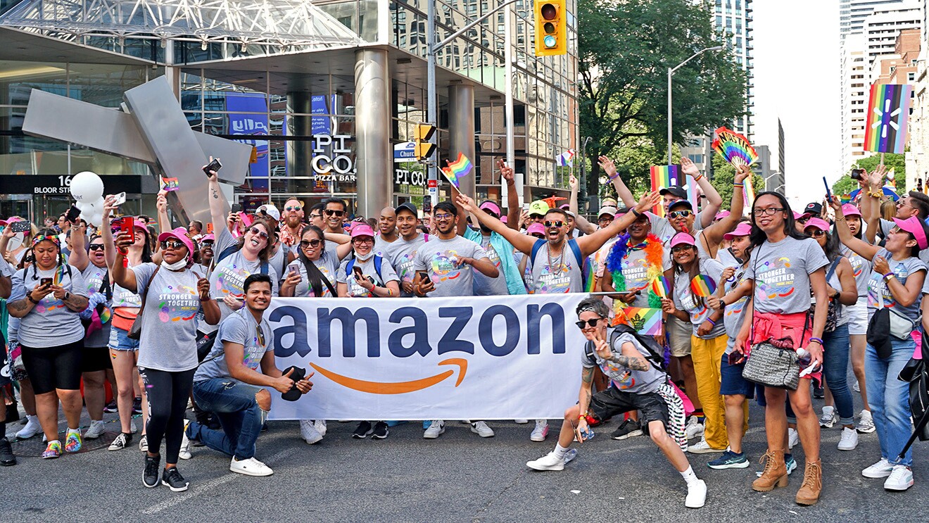 A photo of a crowd of people standing in front of an Amazon banner at the 2022 Amazon Toronto Pride parade.