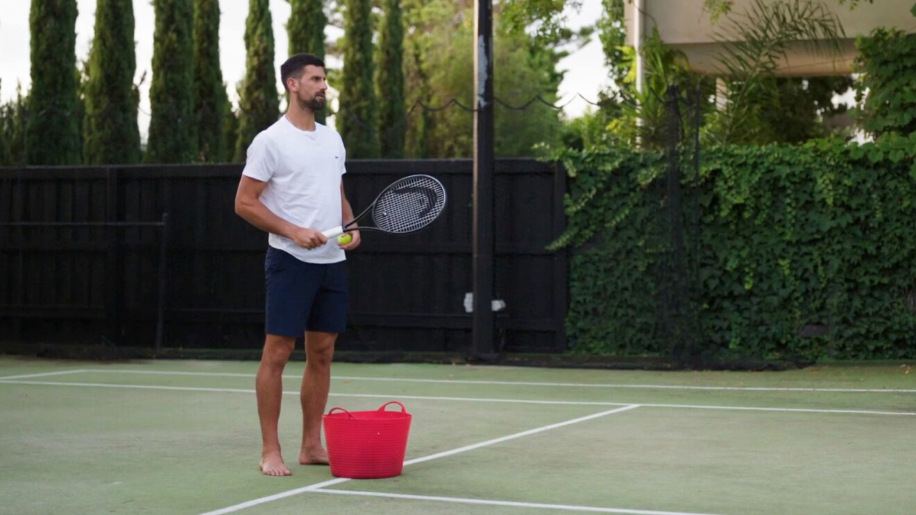 Novak Djokovic on a tennis court with a tennis ball and racket in his hand