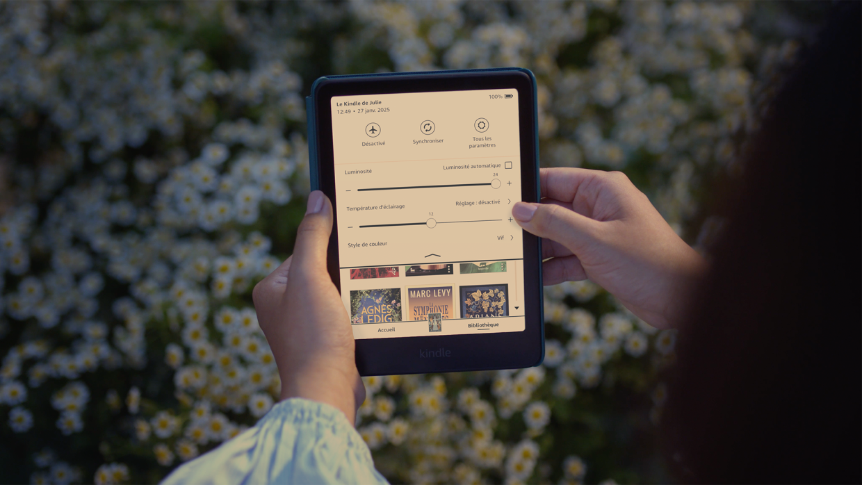 Mains tenant une liseuse Kindle affichant une interface en français sur fond de marguerites
