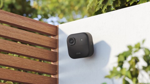 Blink camera secured to a white wall surrounded by greenery