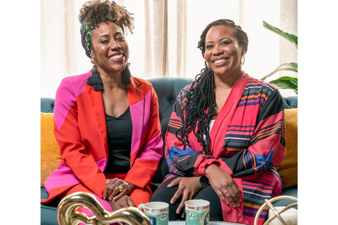 Cara and Jenae smile as they sit next to one another on a couch.