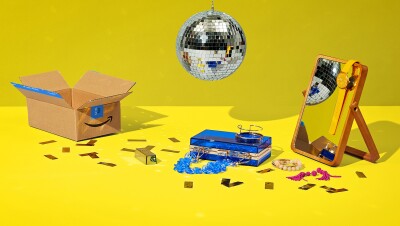 迪斯科球上面漂浮的图像显示的物品。有一个亚马逊盒、塑料、蓝色钱包,一面镜子和一个橙色看挂在上面。地面上有纸屑以及手镯和耳环。所有这一切的背景是明亮的黄色。