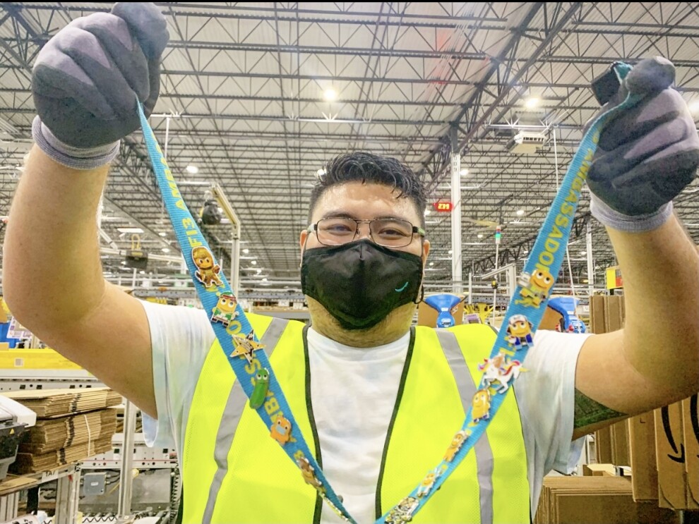 A man, an employee at an Amazon fulfillment center, holds up a lanyard with many pins on it.