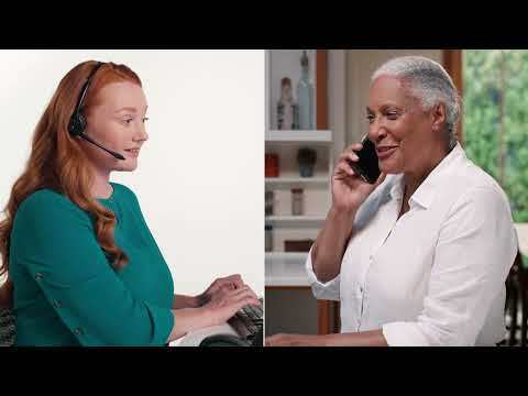 An image of a woman standing in her bathroom in front of a window and her mirror. She is on the phone and looking at a prescription bottle she is holding while smiling. 