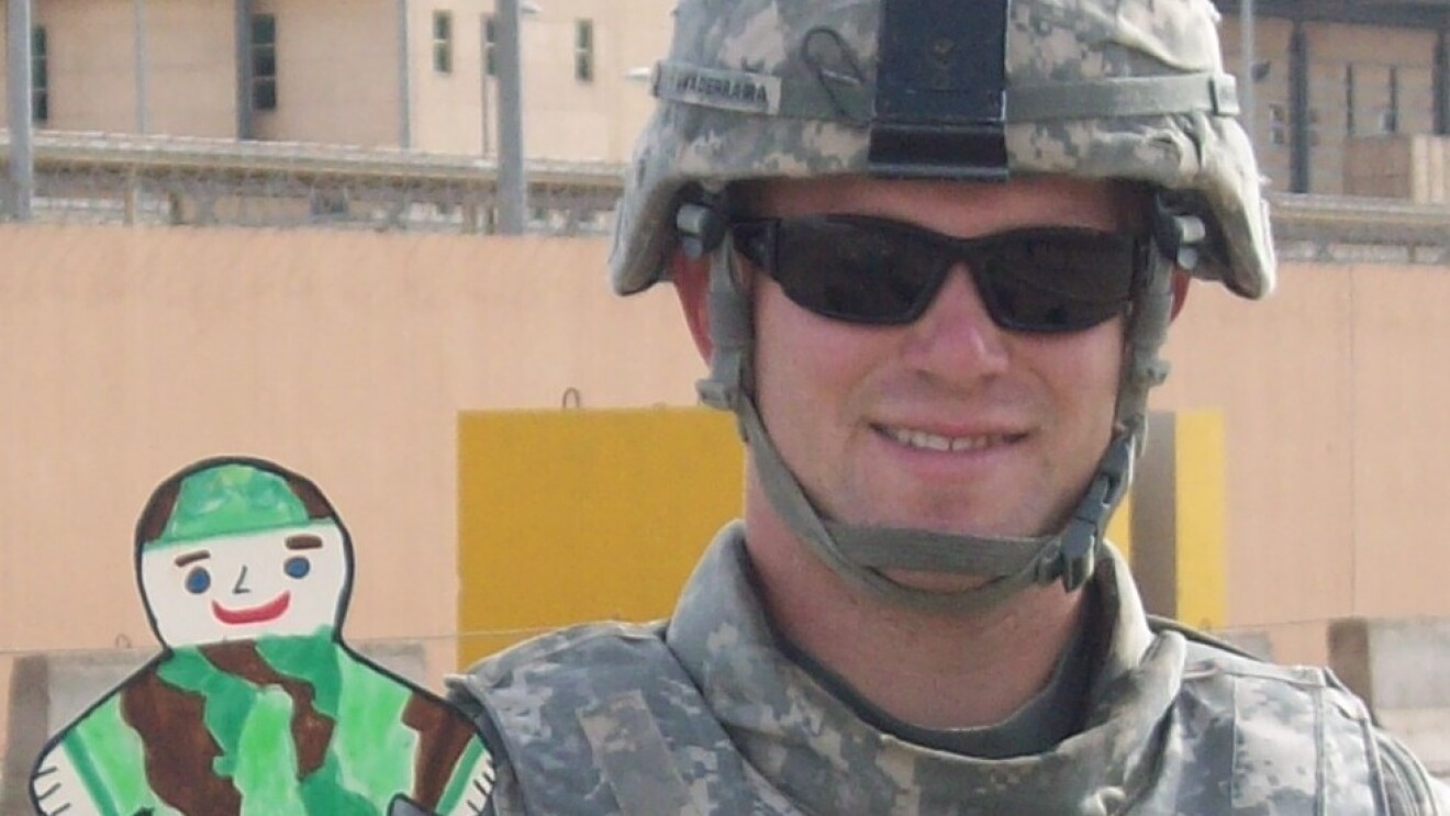 Aaron Guaderrama in combat uniform, holding a child's paper cutout of a soldier in camouflage
