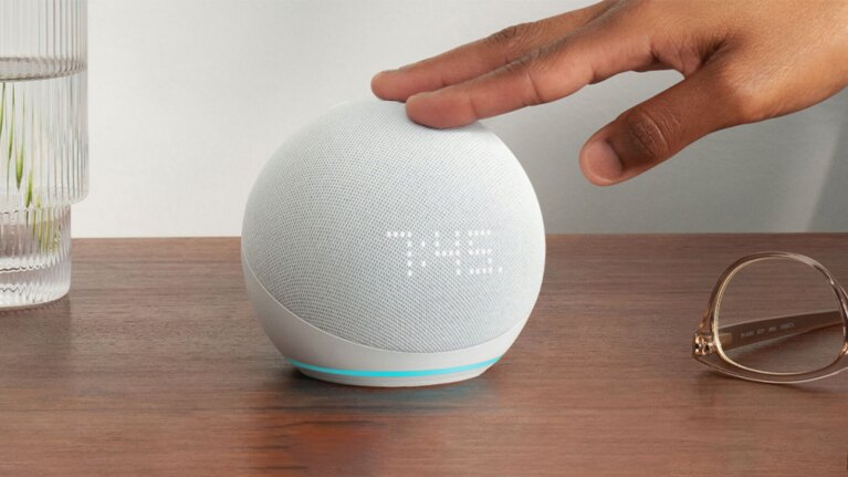 An image of an hand tapping an Amazon Echo device sitting on a nightstand.