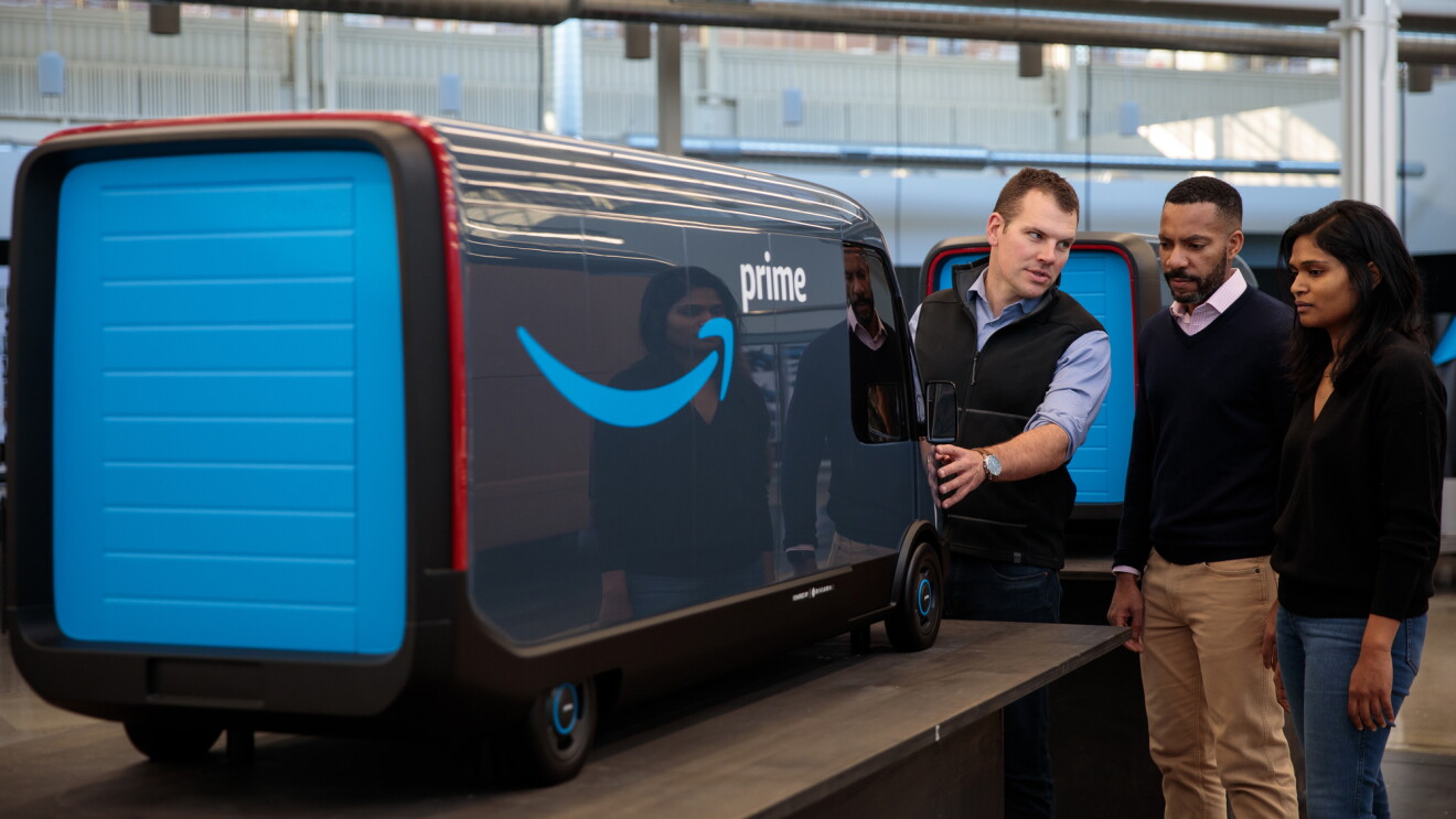 Three people look at a scale model of an electric delivery vehicle with the Amazon smile logo and "Prime" written on the side.