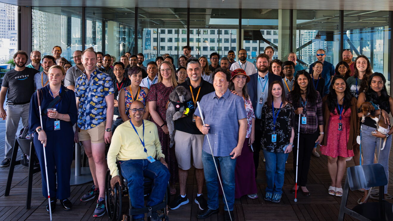 Large team photo showcasing inclusivity with wheelchair user and guide dogs
