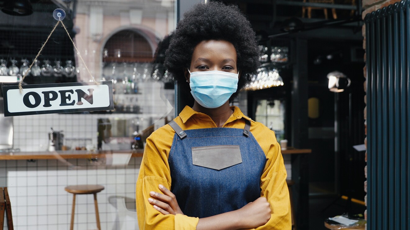 一个戴着面具的黑人女性和牛仔裙站在敞开的门口的餐厅