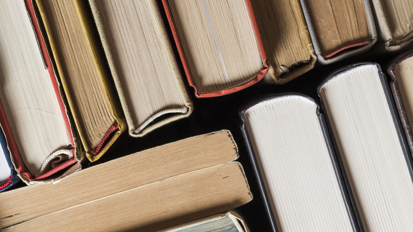 Many hardbound books stacked tightly together at various angles, seen edge on.