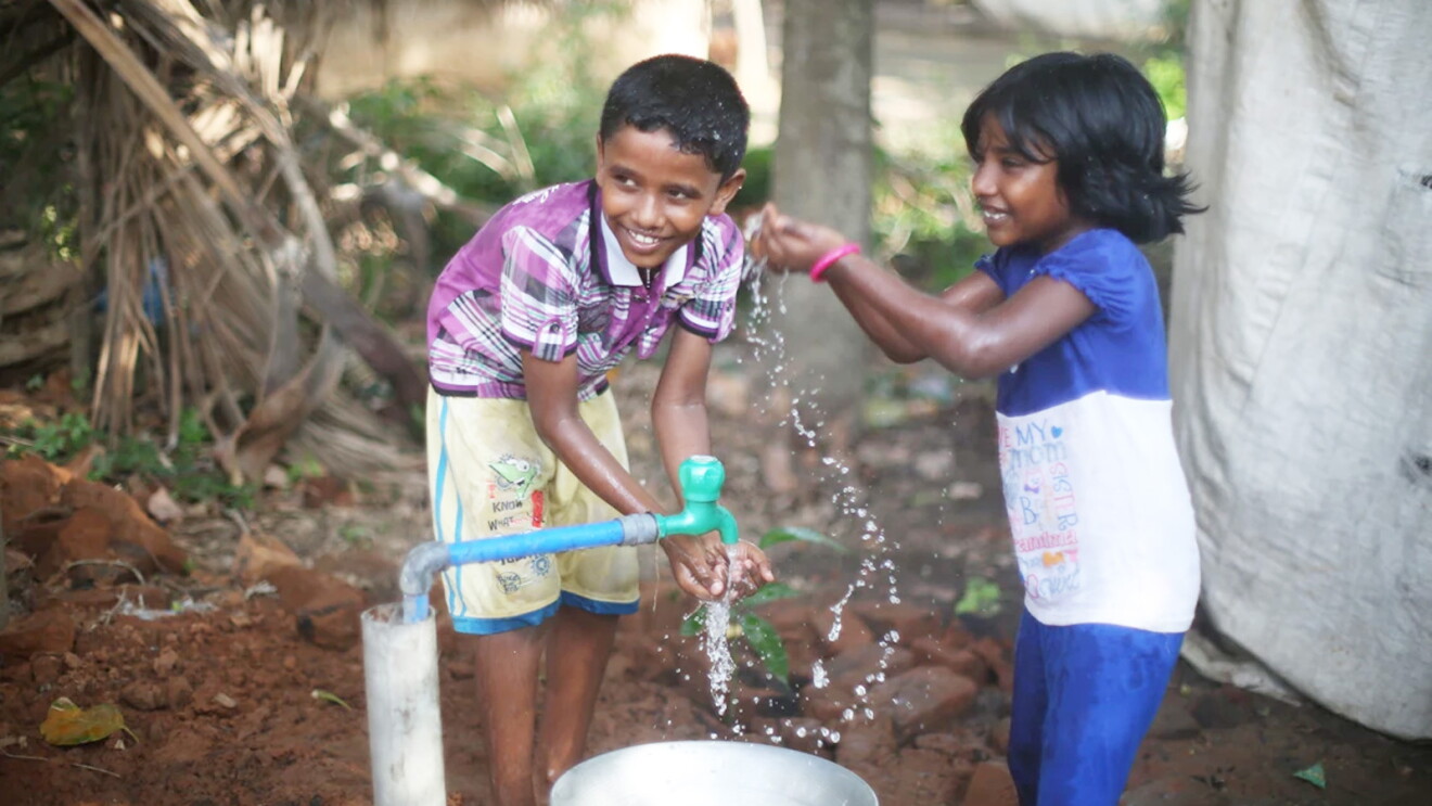 An image of a boy and a girl grabbing water with their hands.
