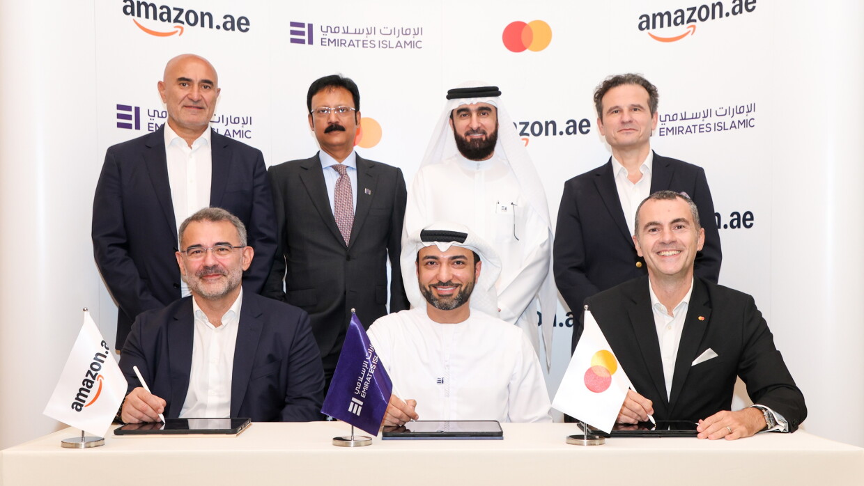 Amazon, Mastercard, EIB employees proudly sign a partnership in front of a cobranded rollup