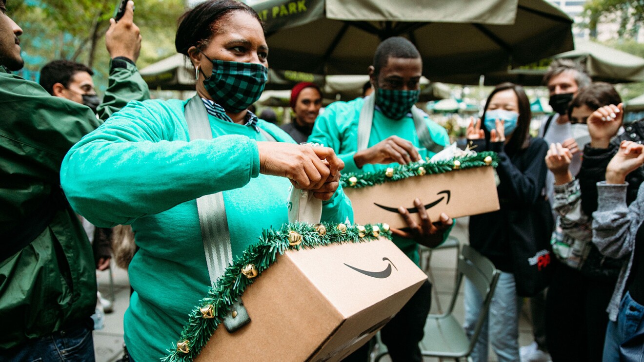 An image of a woman passing out treats to a crowd. She is waring a green Amazon shirt and a black and green checkered face mask.