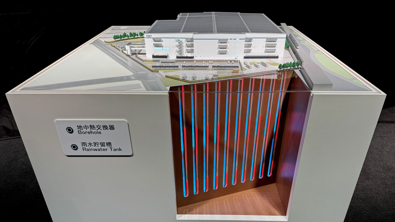 白い台の上に面積が広い4階建ての白い建物の模型。その建物の下に垂直に赤と青い線が伸びている