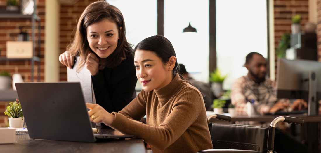 Two women working together, looking at a laptop 