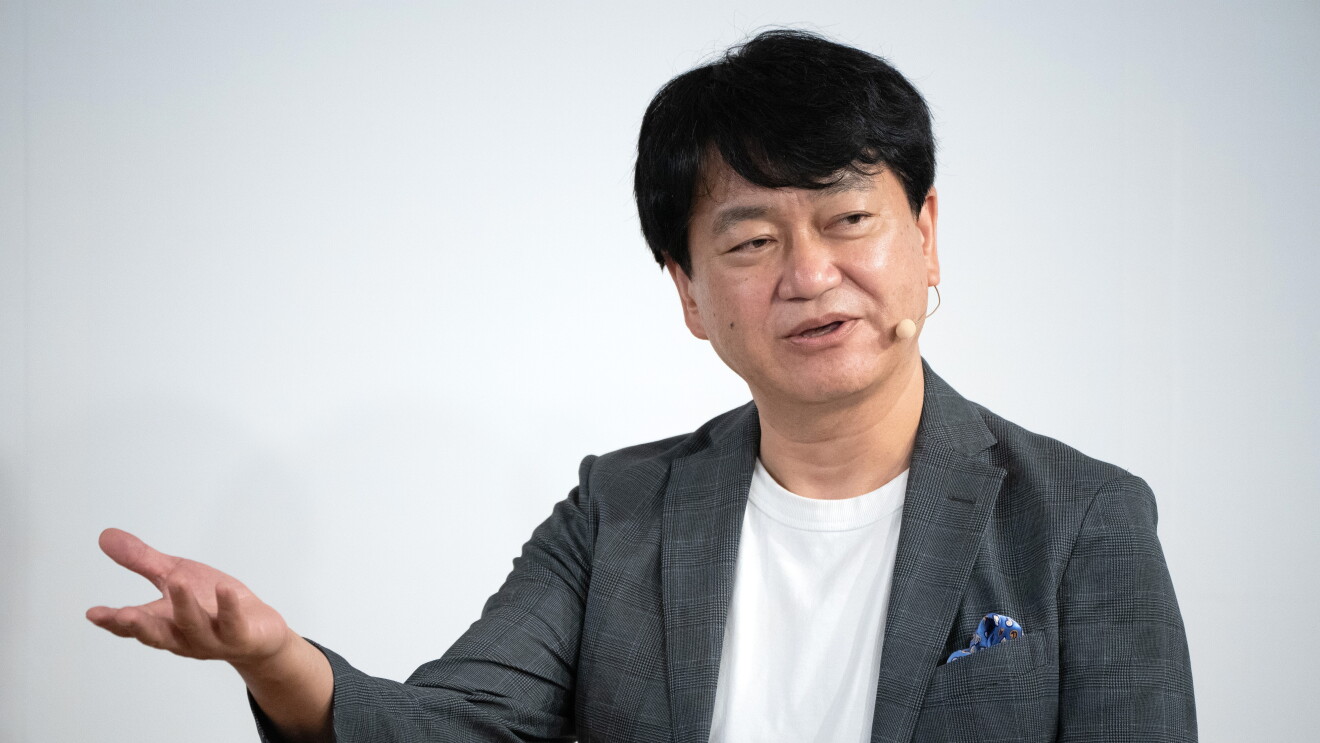 右手のてのひらを上に向けているジェスチャーしている男性が右側に向かって話しかけている。彼は白いTシャツにグレーのジャケットを着ている（角井亮一氏）