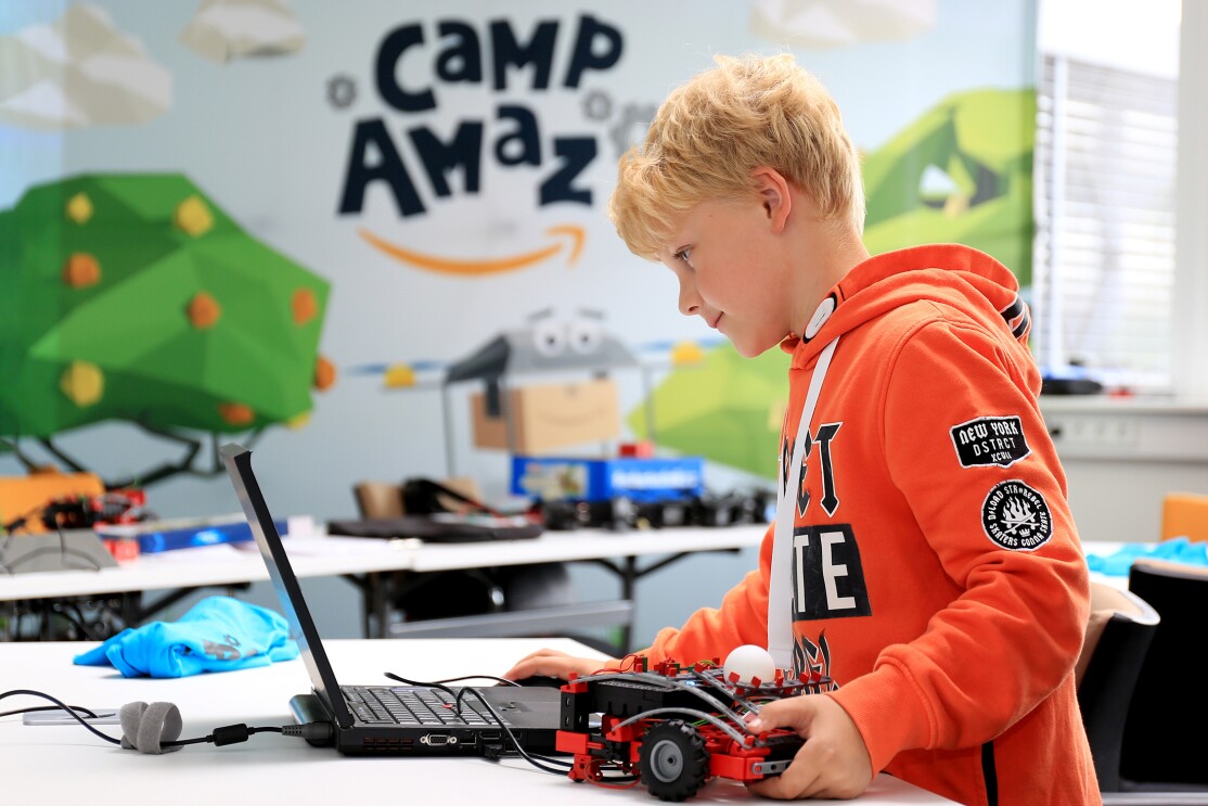 Ein blonder Junge im orangenen Hoodie blickt auf einen Laptop, neben ihm ein Fischetechnik-Transportfahrzeug