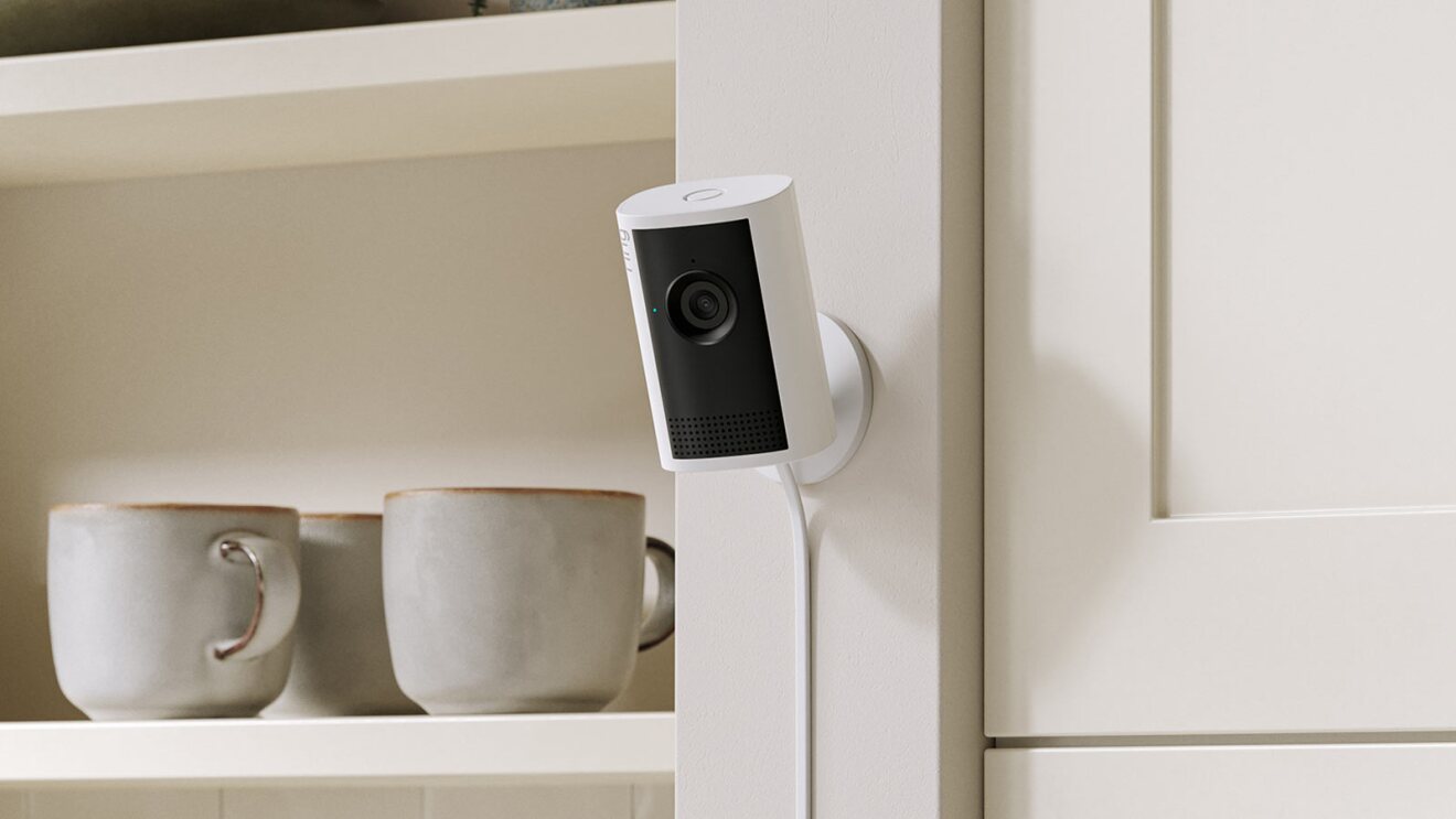 Smart home camera mounted next to kitchen shelves with coffee mugs
