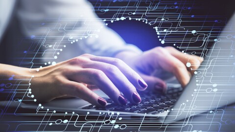 A woman's hands hover over a laptop as she works