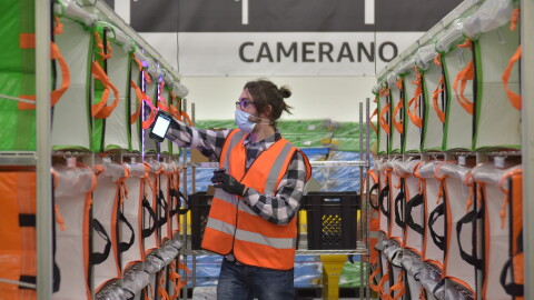 Un corridoio di pacchi in un magazzino Amazon. Al centro un dipendente smista i pacchi, sullo sfondo si legge la scritta Camerano