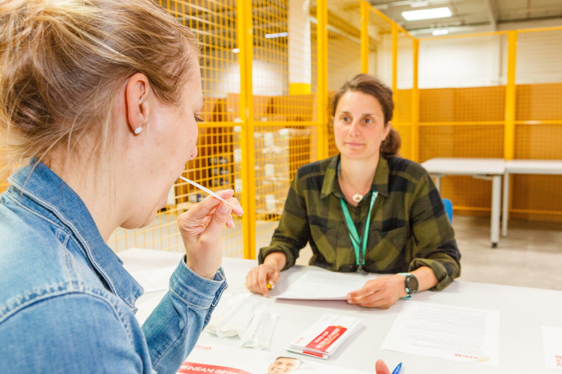 Eine blonde Mitarbeiter lässt sich typisieren - vor ihr hält eine weitere Mitarbeiterin die DKMS-Formulare bereit