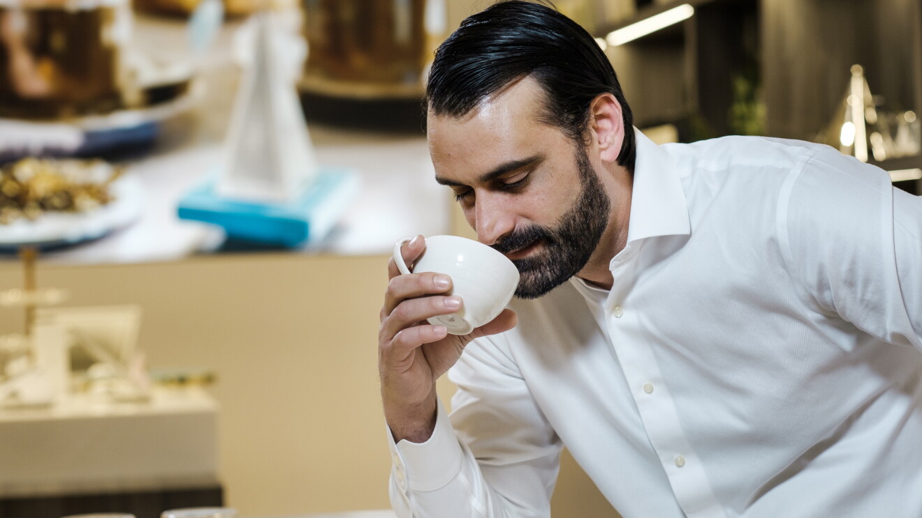 A man holds a tilted cup to his nose to take in the aroma of freshly brewed tea.