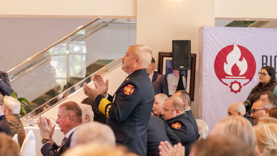 Firefighters applauding at formal event with Amazon with department logo banner