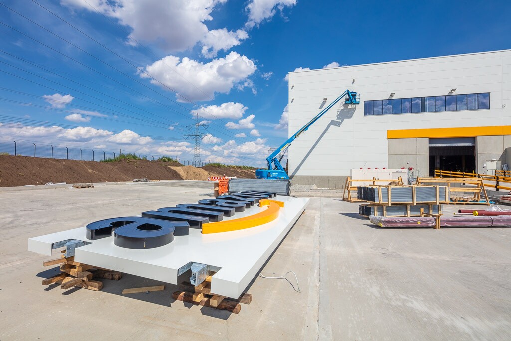 Ein Schild mit Logo liegt auf dem Außengelände vor dem Gebäude.