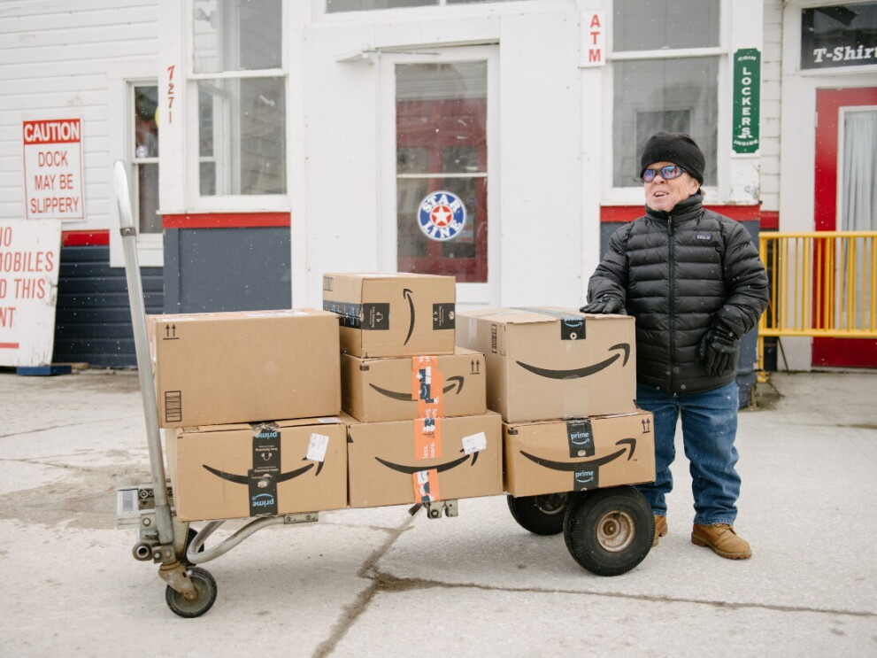 Sara stands next to a trolley stacked with Amazon boxes.