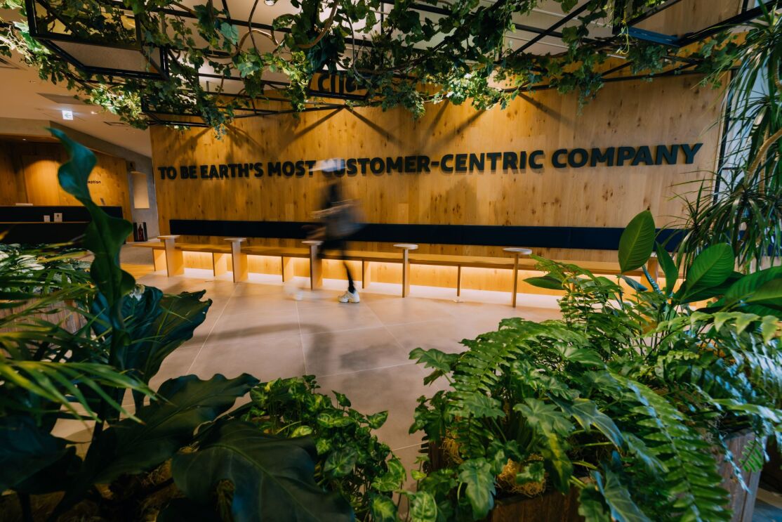 植物がある空間の壁にTo Be Earth‘s Most Customer - Centric Companyの文字。その前を人が歩いている