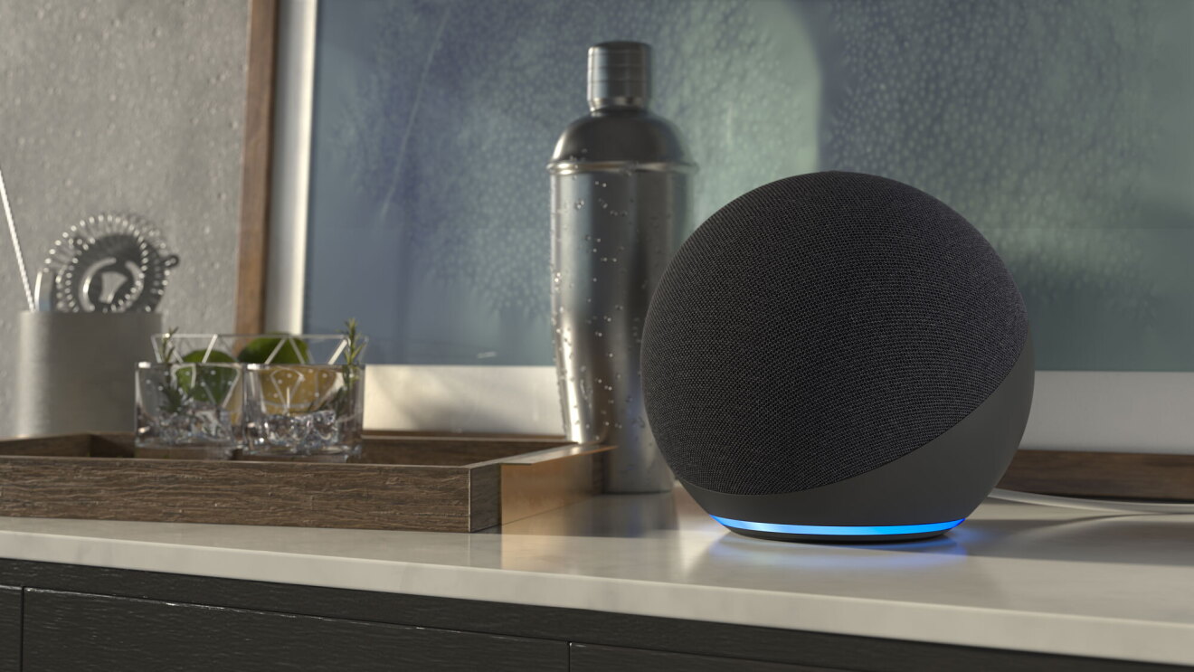 An Echo device sits on a table next to a cocktail shaker and two cocktail glasses.