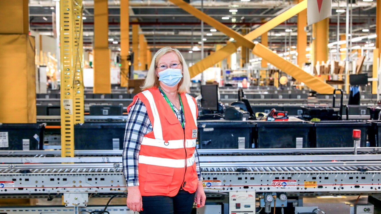Carole Wee standing in front of a conveyor belt in a fulfilment centre.