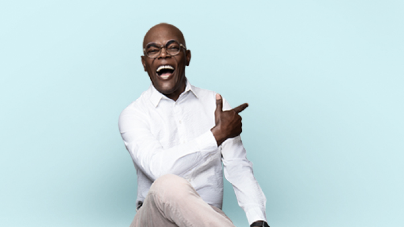 Samuel L. Jackson is laughing, sitting on a stool, and posing for a photo.