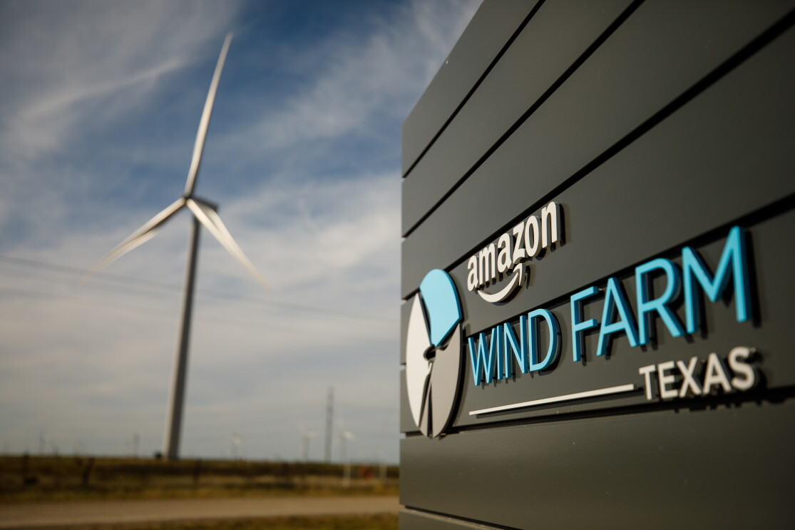 A sign says 'Amazon Wind Farm Texas.' A wind turbine is in the background.
