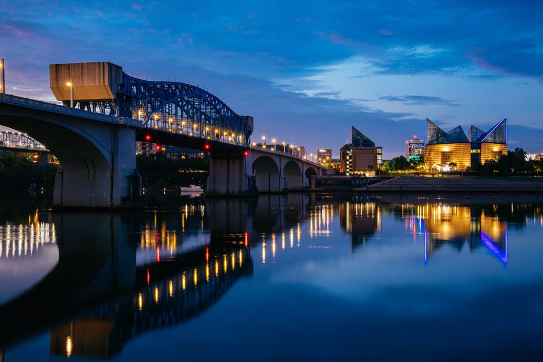 The Tennessee river at night, with a bridge stretching along it's width. In the foreground, Chattanooga buildings are lit up.