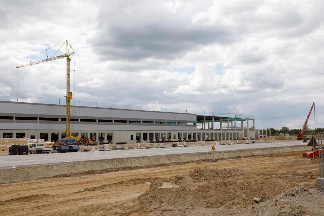 Bagger, Kräne und Baustellenfahrzeuge sind vor einem lang gestreckten Gebäude