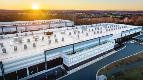 An aerial photo of an AWS data center in Northern Virginia. Behind the data center is a horizon line with the sun rising.