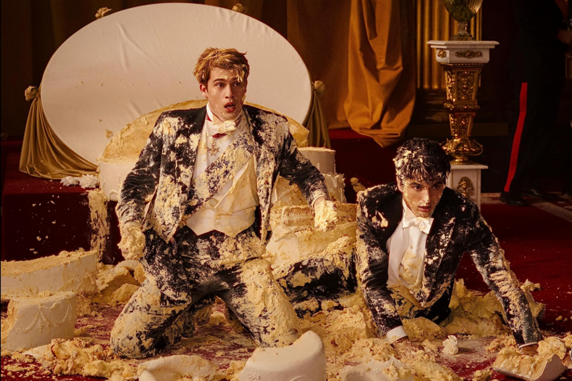 Two men wearing formal suits kneeling on the floor covered in cake