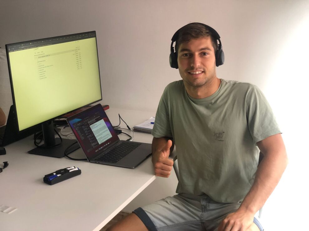 An image of a man smiling for a photo at his computer while giving a "thumbs up."