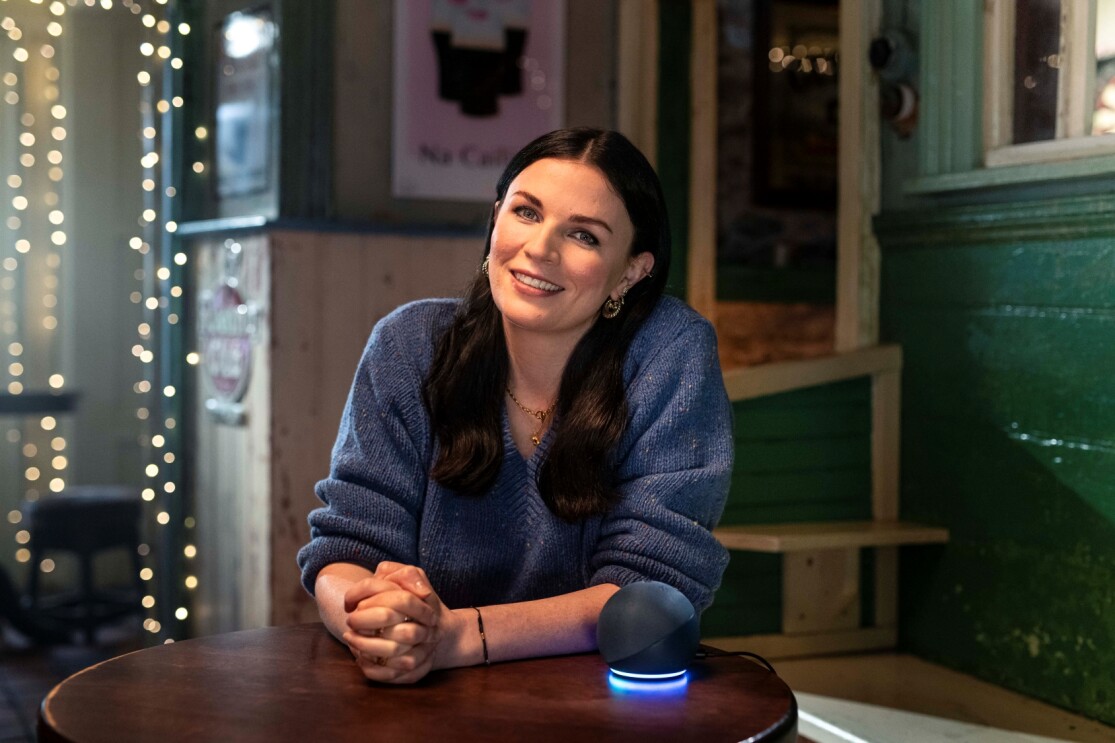 Aisling Bea sitting at a table talking with an Amazon Alexa Device