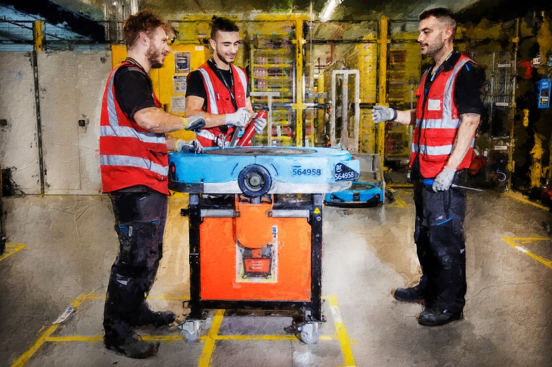 Fotomontaje. Es una fotografía que lleva un filtro que simula un cuadro pintado. Aparecen tres hombres de pie vestidos con un chaleco rojo y pantalón negro con botas de seguridad. Los tres están alrededor de una mesa con un robot que están reparando. De fondo estanterías de color amarillo. El hombre de la izquierda está con un tornillo reparando el robot.