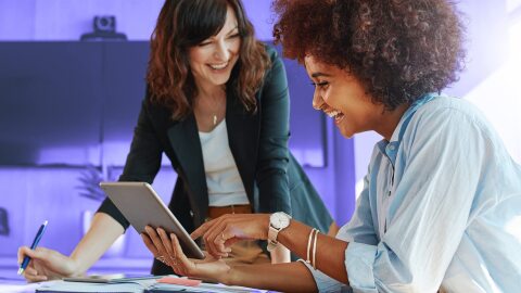Due donne conversano mentre osservano un tablet.