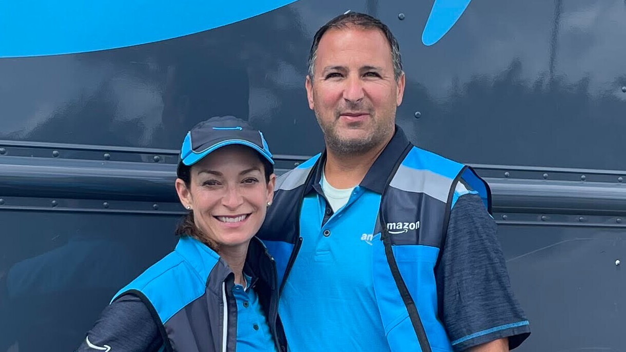 Alison Gatto and her husband wear blue Amazon uniforms and pose in front of a delivery vehicle.