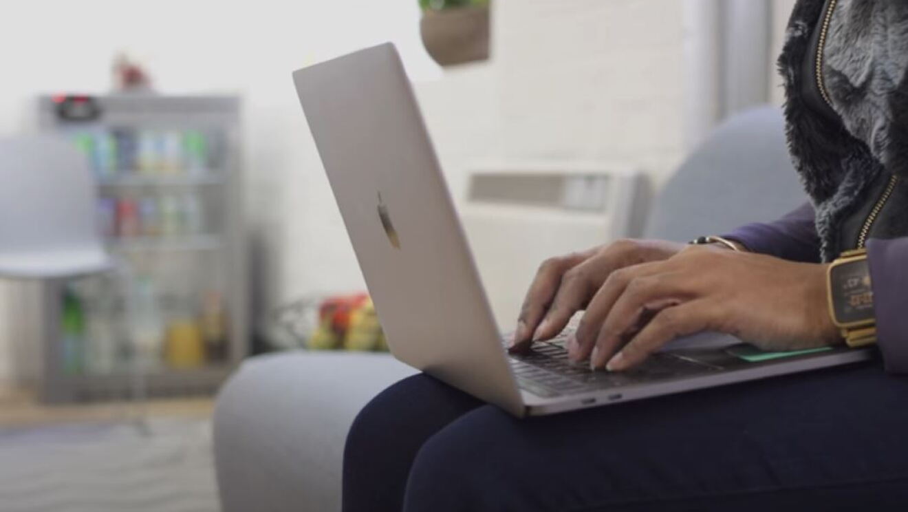 A woman types on the keyboard of a laptop computer while sitting on a sofa. 