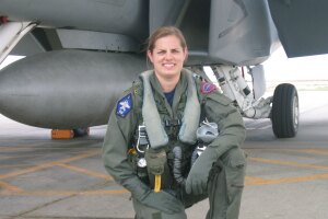 An image of Sarah Rhoads in her pilot gear kneeling in front of a large plane and smiling for a photo.