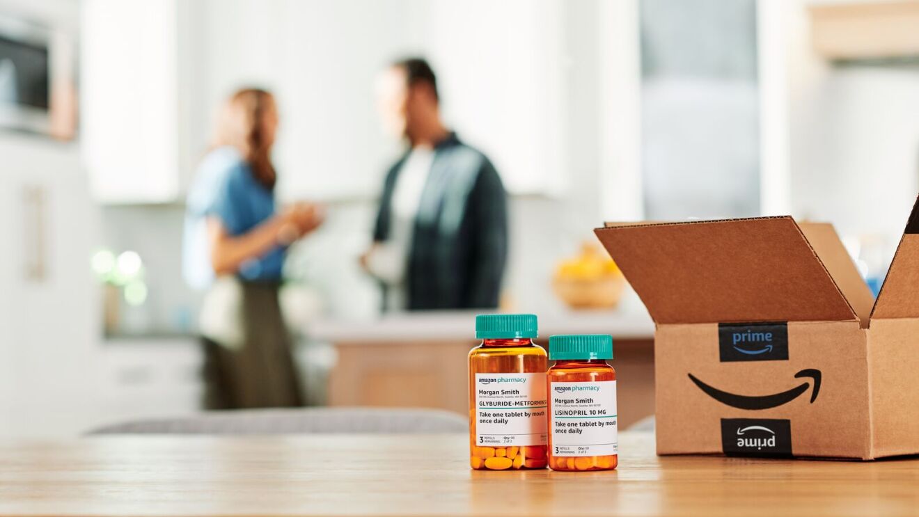Prescription bottles and Amazon Prime box on table, people chatting in background.