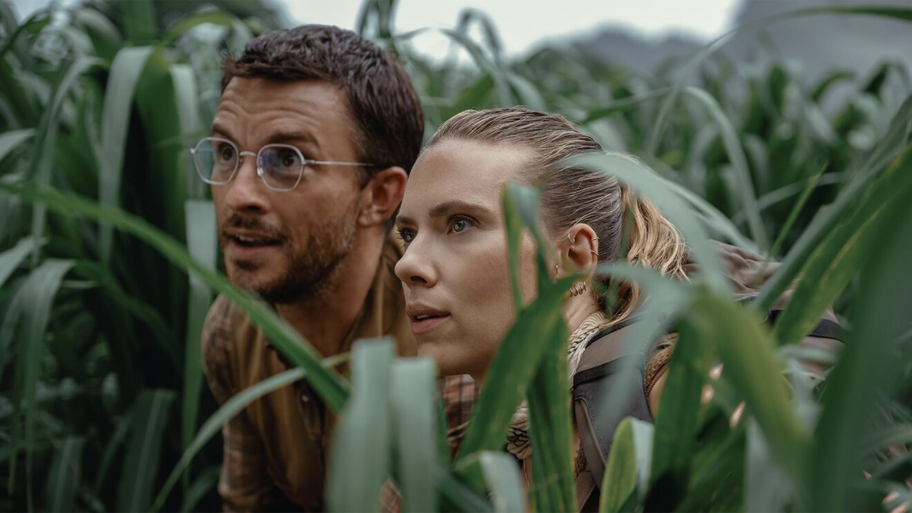 Jonathan Bailey and Scarlett Johansson crouching in grass in 'Jurassic World Rebirth.'