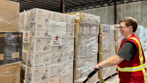 A volunteer wears a safety vest and smiles as they move a pallet of items being donated with a machine.